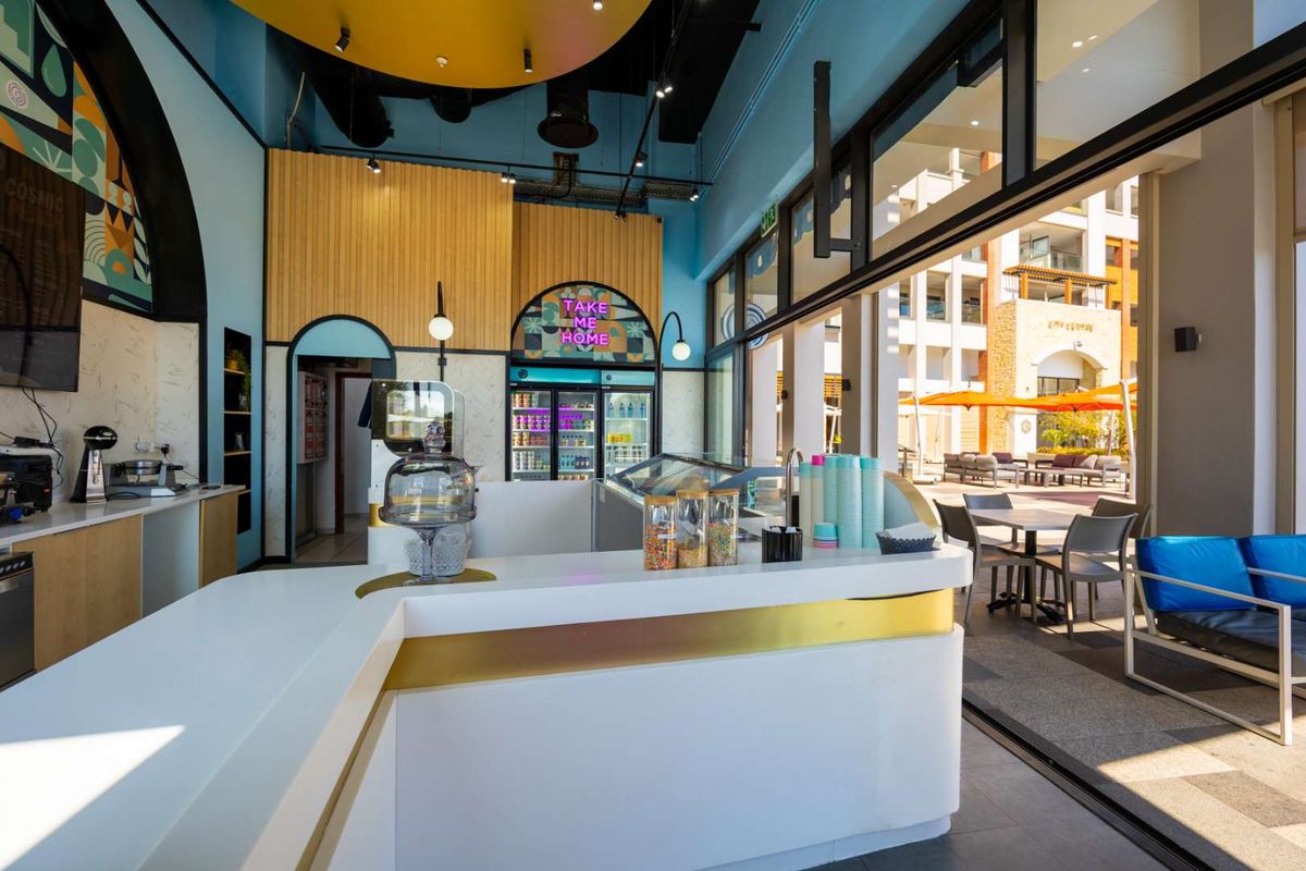Modern open-plan commercial space featuring a sleek service counter, commercial refrigeration, and large sliding glass doors opening to an outdoor seating area.