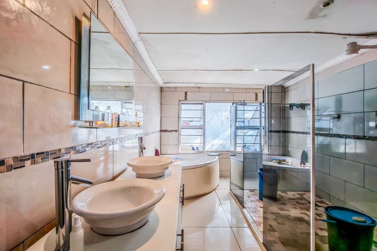 A spacious bathroom featuring dual vessel sinks, a corner soaking tub, and a glass-enclosed shower area with tiled walls and flooring.