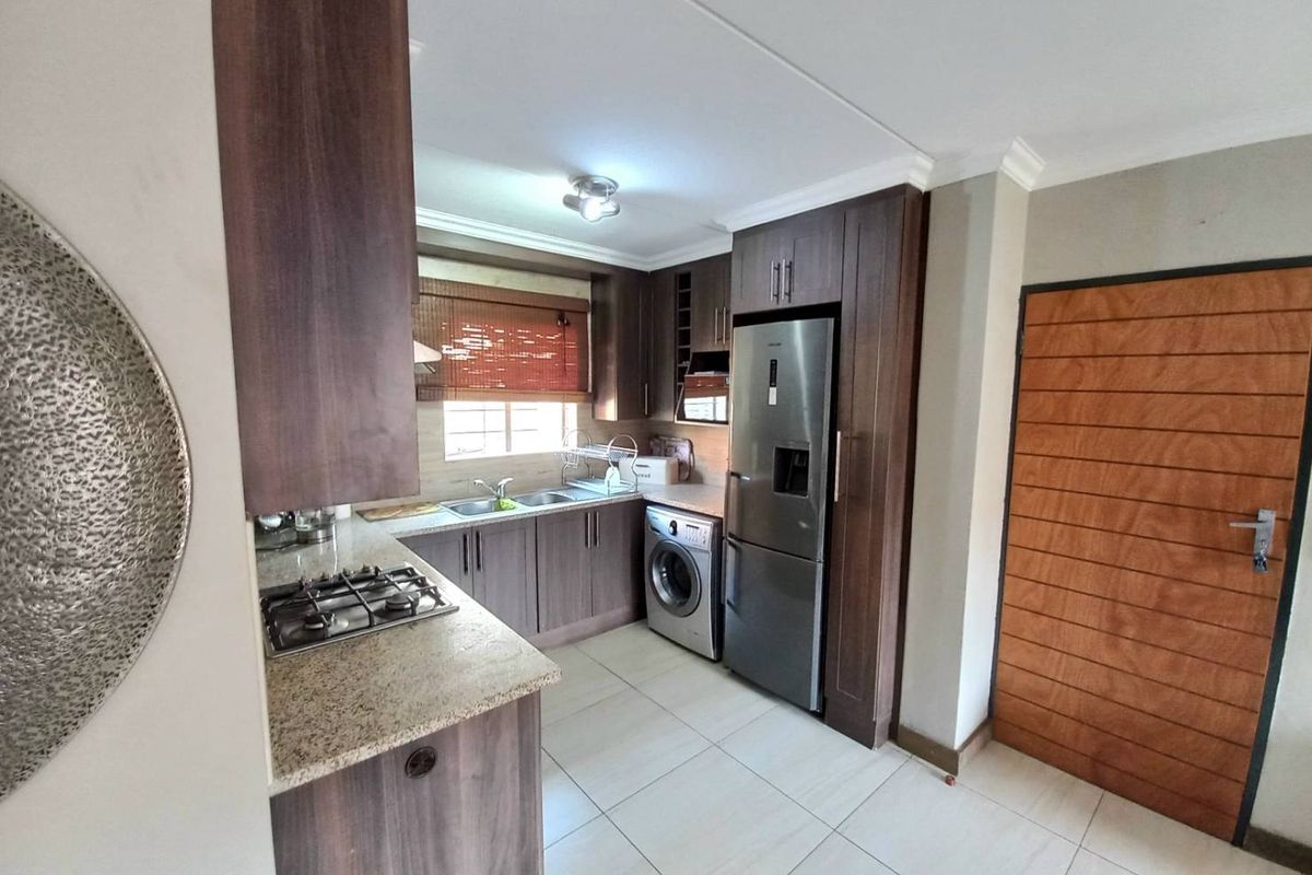 A functional kitchen featuring dark wood cabinetry, granite countertops, a built-in gas hob, and integrated space for a washing machine and refrigerator.