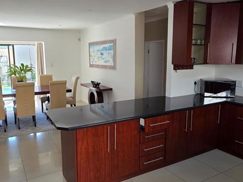 Open plan kitchen and dining area featuring dark wood cabinetry, granite countertops, and neutral tiled flooring throughout.