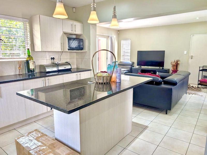 Open-plan living area featuring a modern kitchen with a central island, granite countertops, and tiled flooring, seamlessly flowing into the adjacent lounge space.