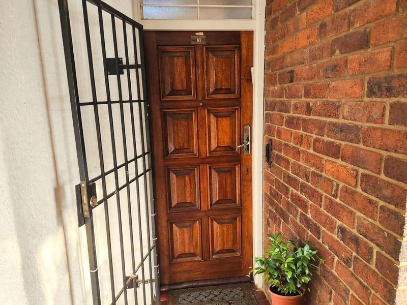 A secure apartment entrance featuring a solid timber front door protected by a black metal security gate, set within a classic brick facade.