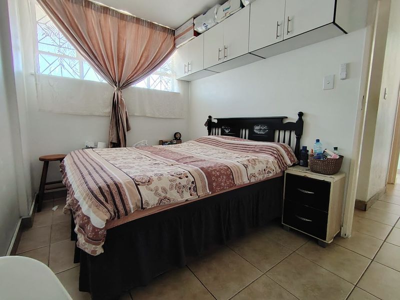 A functional bedroom featuring built-in overhead storage cabinetry, tiled flooring, and a window with security bars.