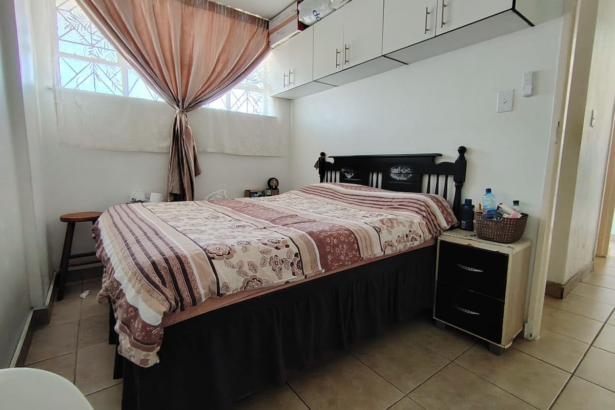 A functional bedroom featuring built-in overhead storage cabinetry, tiled flooring, and a window with security bars.