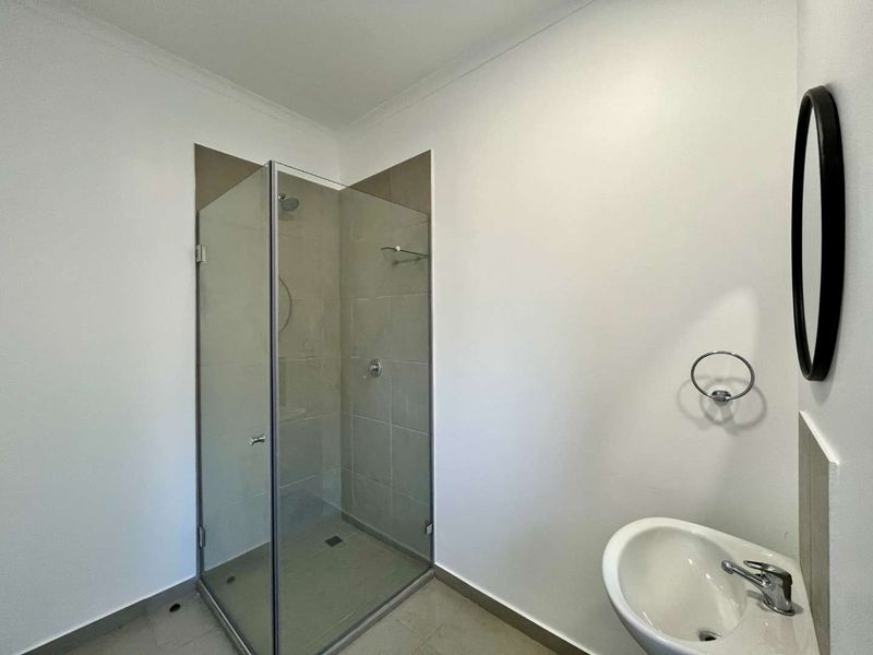 A clean, modern bathroom featuring a glass-enclosed shower, wall-mounted basin with chrome fixtures, and neutral floor tiling.
