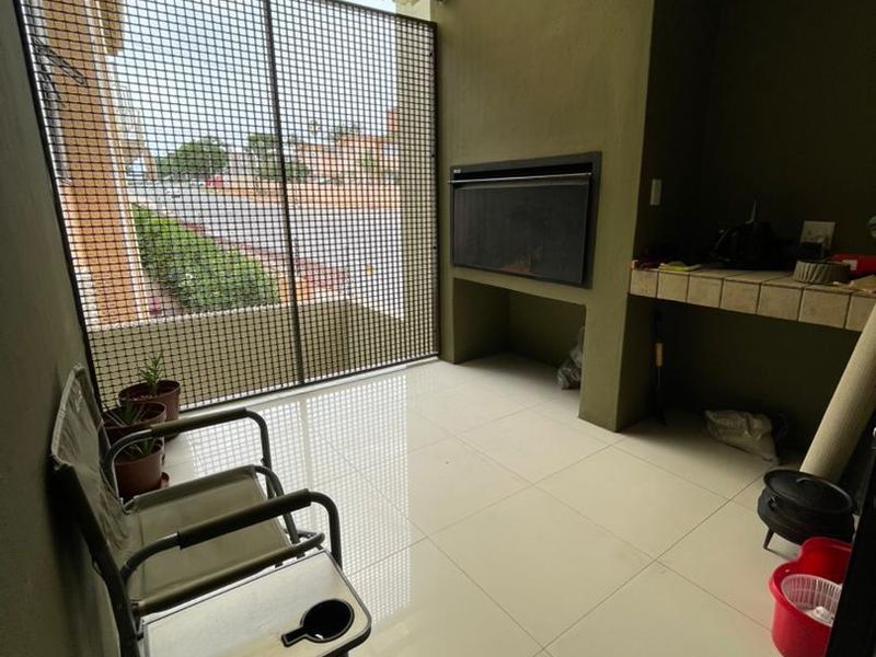 Covered patio area featuring a built-in braai, tiled flooring, and a security mesh screen, providing a functional outdoor entertainment space.