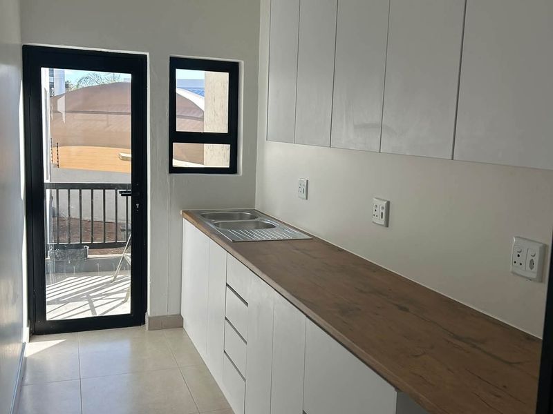 A clean, modern scullery featuring white built-in cabinetry, a wood-look laminate countertop, stainless steel sink, and direct access to an outdoor area.