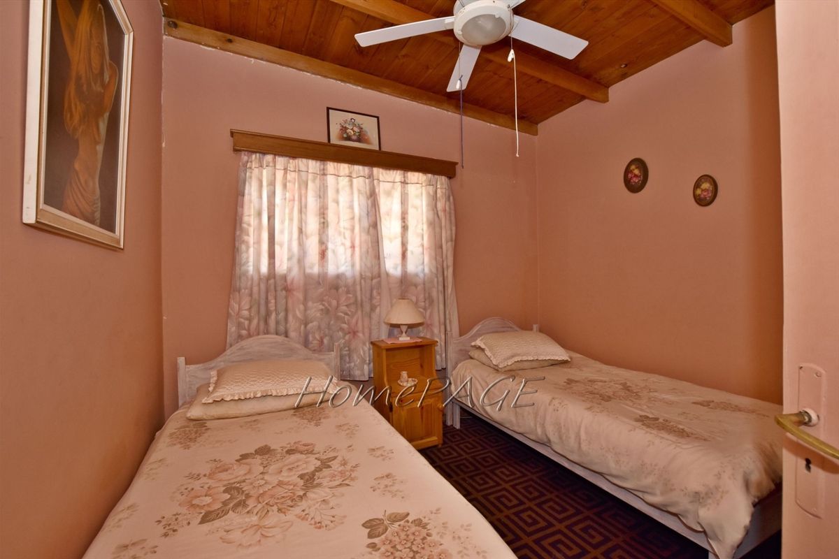 A bedroom featuring a vaulted timber ceiling with a fitted ceiling fan and a window with curtain pelmet.