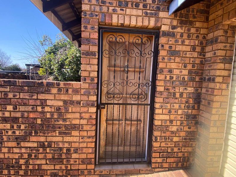 A secure entrance featuring a timber door protected by a decorative wrought iron security gate, set within a face brick exterior wall.