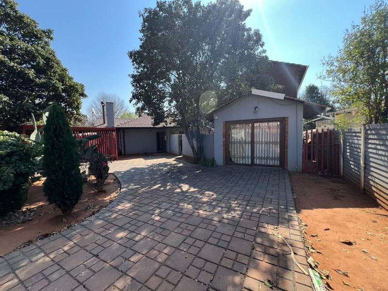 Front exterior view of the property featuring a paved driveway, a sliding glass door with security gate, and established garden surroundings.