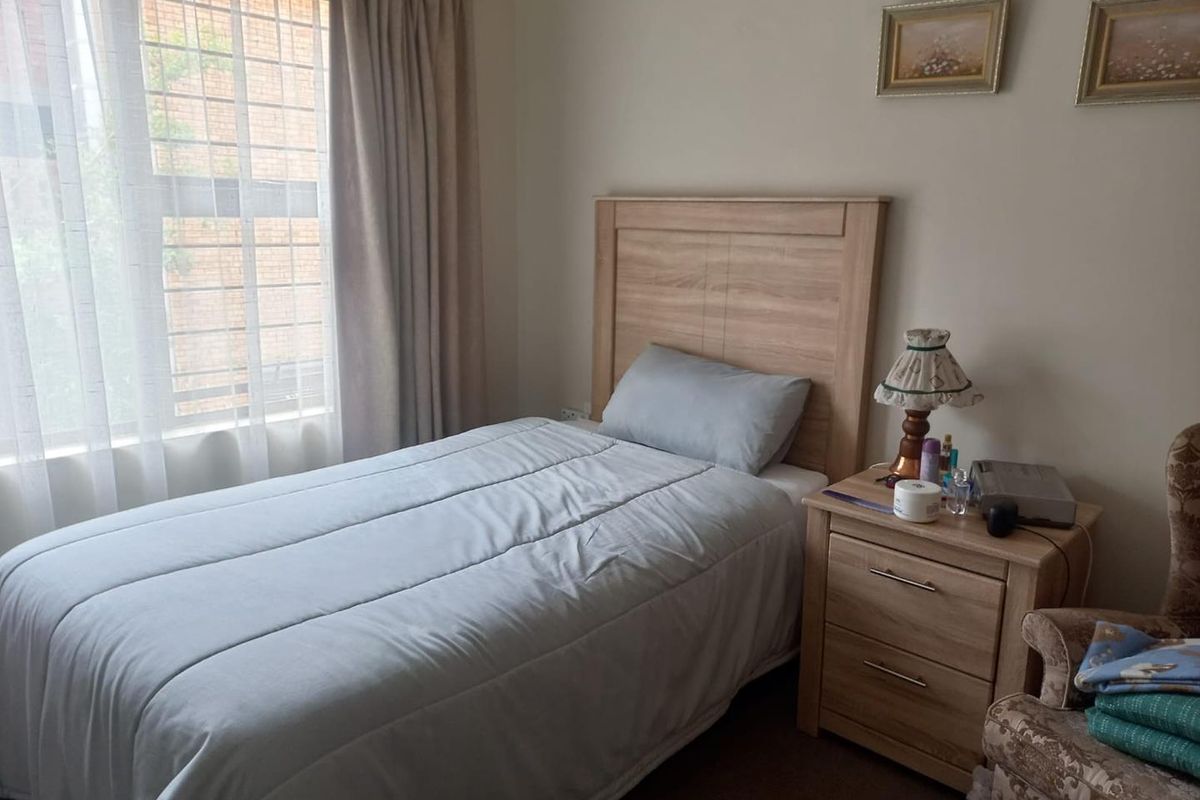 A functional bedroom featuring neutral wall tones, carpeted flooring, and a large window with fitted curtain tracks.