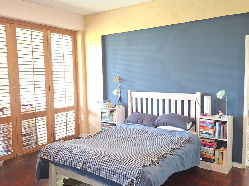 Spacious bedroom featuring warm wooden parquet flooring, large wooden shutter doors for natural light, and direct access to an en-suite bathroom.