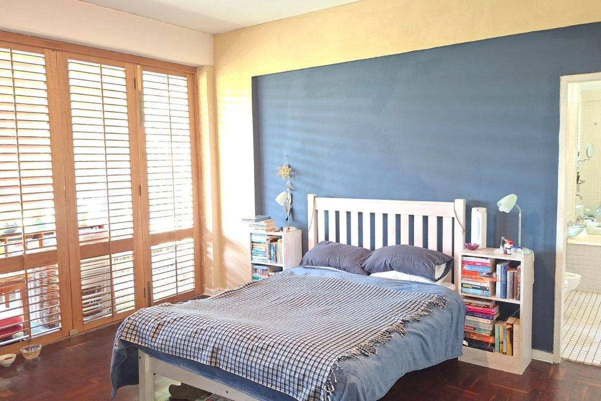 Spacious bedroom featuring warm wooden parquet flooring, large wooden shutter doors for natural light, and direct access to an en-suite bathroom.