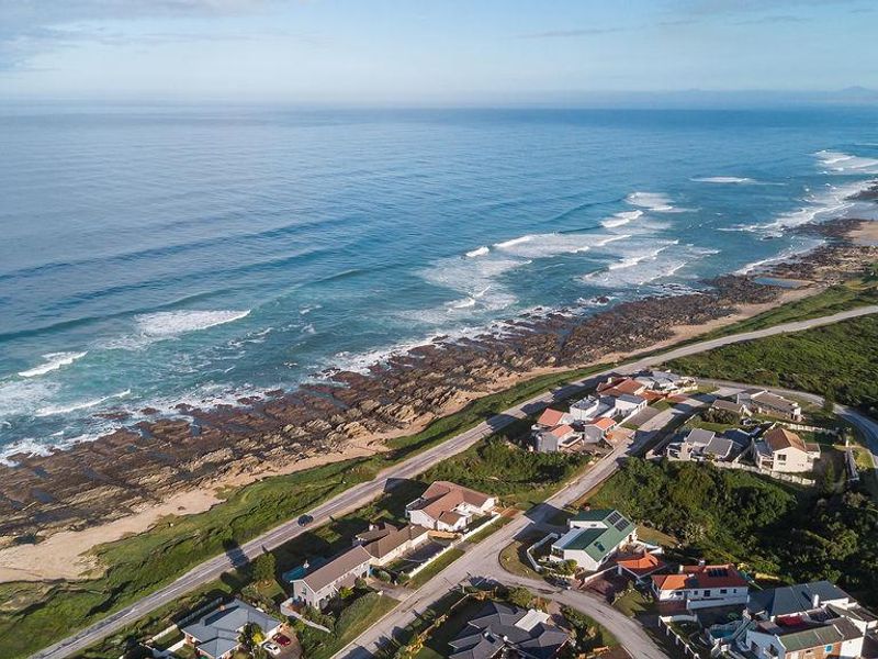 An aerial view of a coastal residential estate situated along the shoreline, showcasing the proximity to the ocean and surrounding natural landscape.