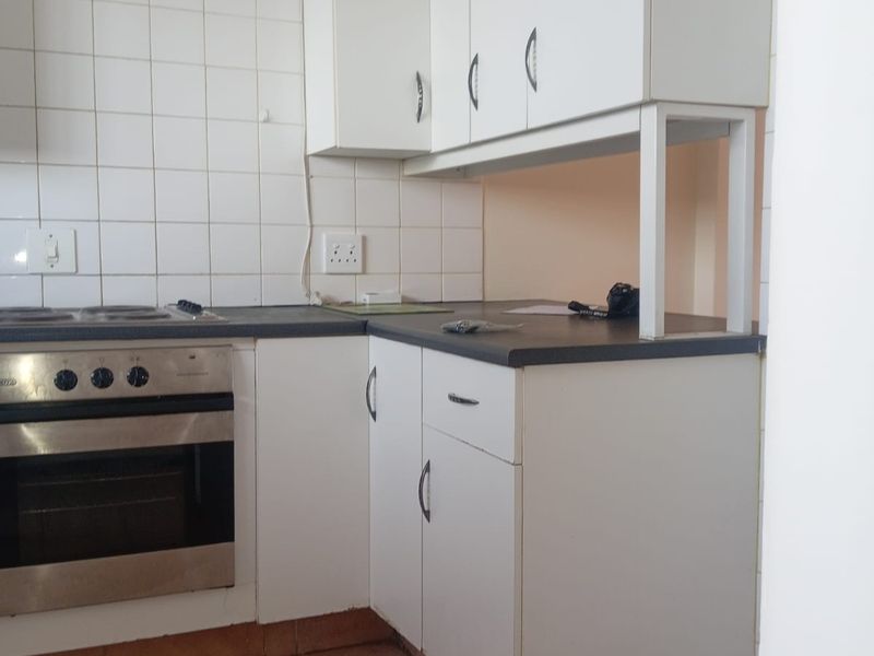 A compact kitchen featuring white cabinetry, dark laminate countertops, a built-in oven, and tiled backsplash, requiring minor repairs to base cabinetry.