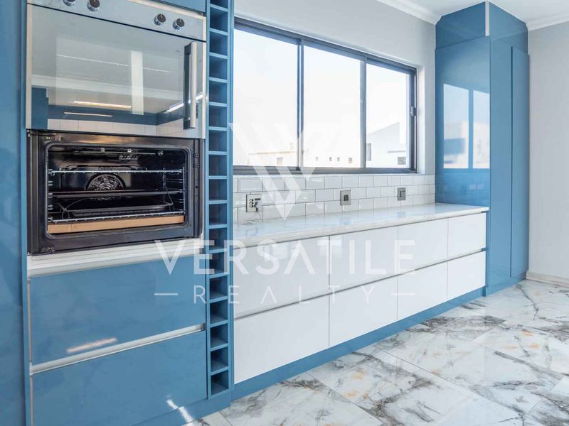 Modern kitchen featuring glossy blue cabinetry, white quartz countertops, subway tile backsplash, built-in oven and microwave, and elegant marble-look floor tiles.