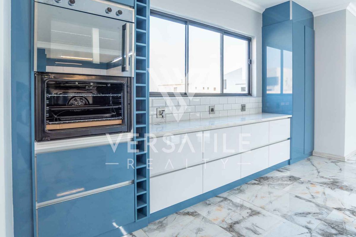 Modern kitchen featuring glossy blue cabinetry, white quartz countertops, subway tile backsplash, built-in oven and microwave, and elegant marble-look floor tiles.