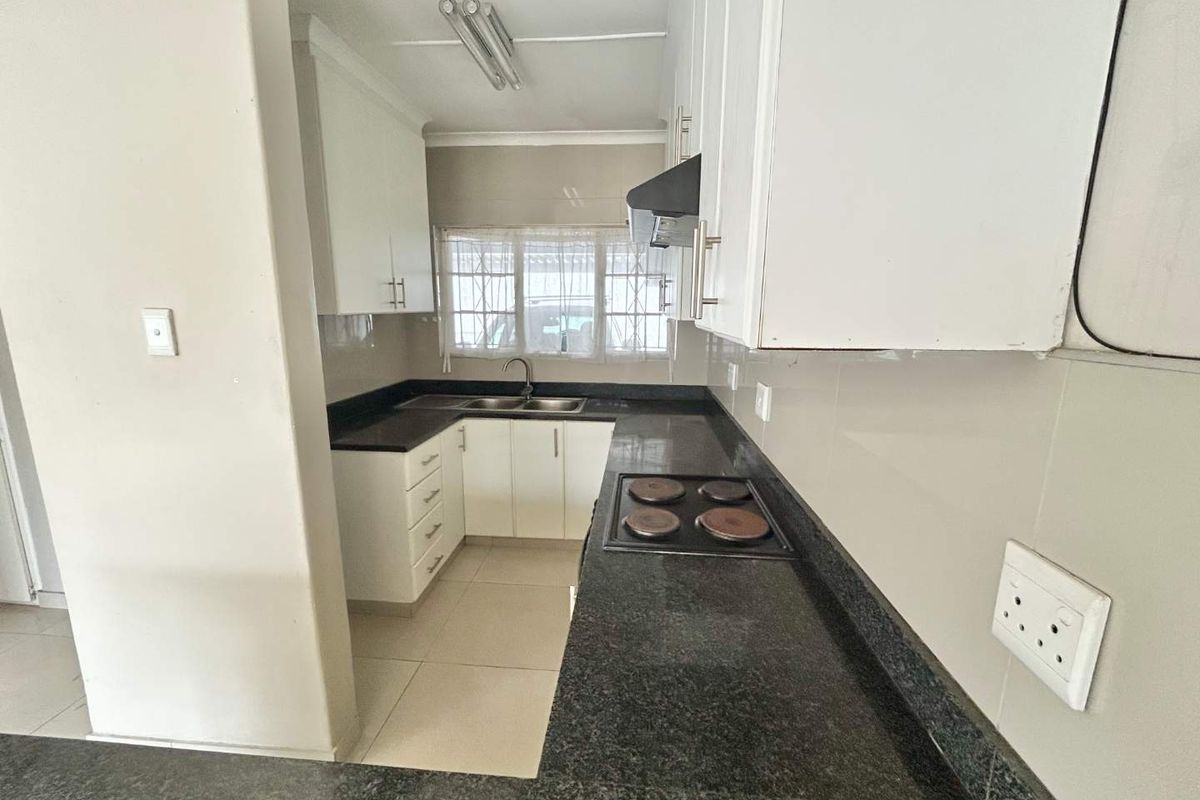 Functional kitchen featuring white cabinetry, dark granite countertops, a built-in electric hob, and a stainless steel double sink.