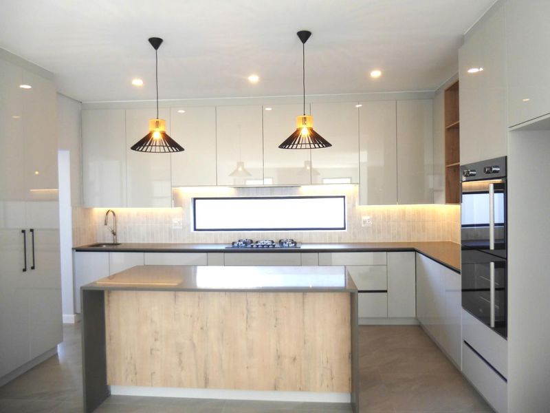 Modern kitchen featuring high-gloss cabinetry, stone countertops, a central island, built-in oven, gas hob, and integrated under-cabinet lighting.