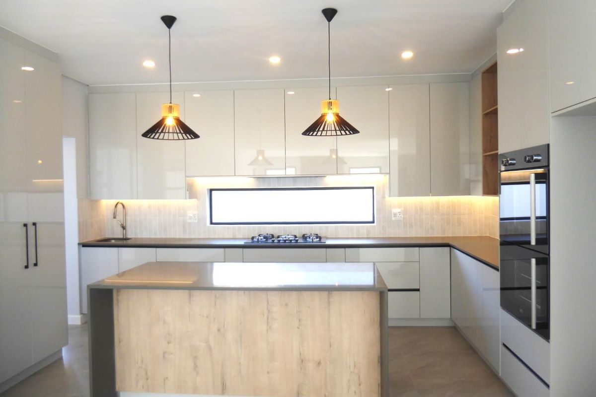 Modern kitchen featuring high-gloss cabinetry, stone countertops, a central island, built-in oven, gas hob, and integrated under-cabinet lighting.