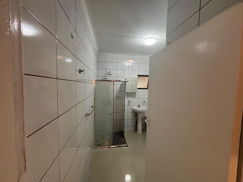 A functional bathroom featuring a glass shower enclosure, pedestal basin, and full-height wall tiling.