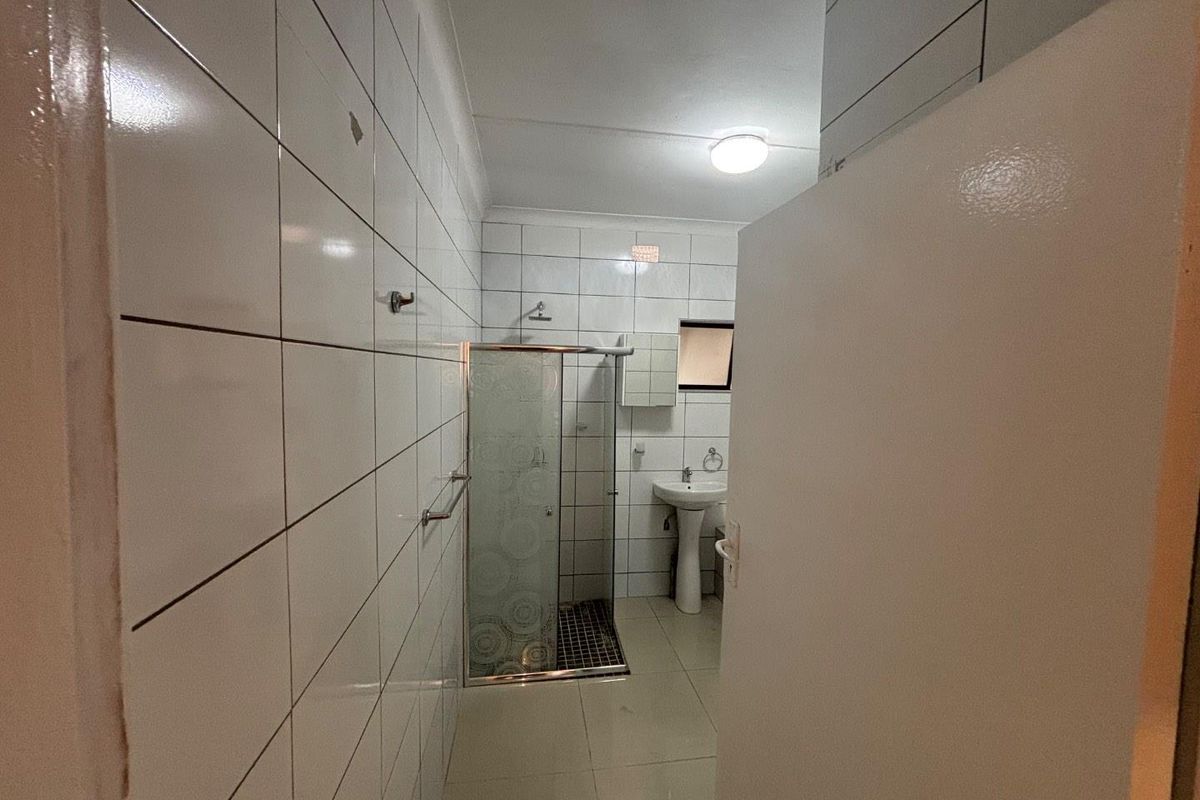 A functional bathroom featuring a glass shower enclosure, pedestal basin, and full-height wall tiling.