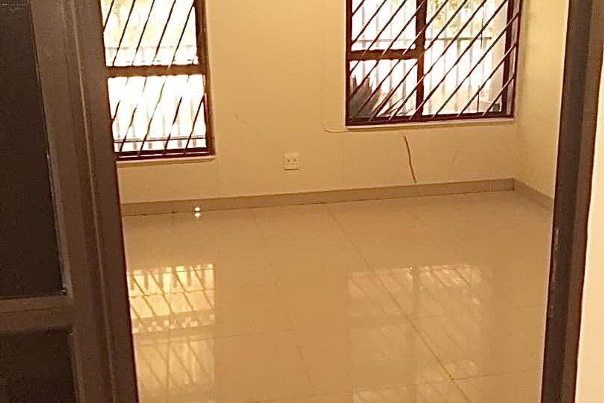 An empty bedroom featuring tiled flooring and windows fitted with security bars.