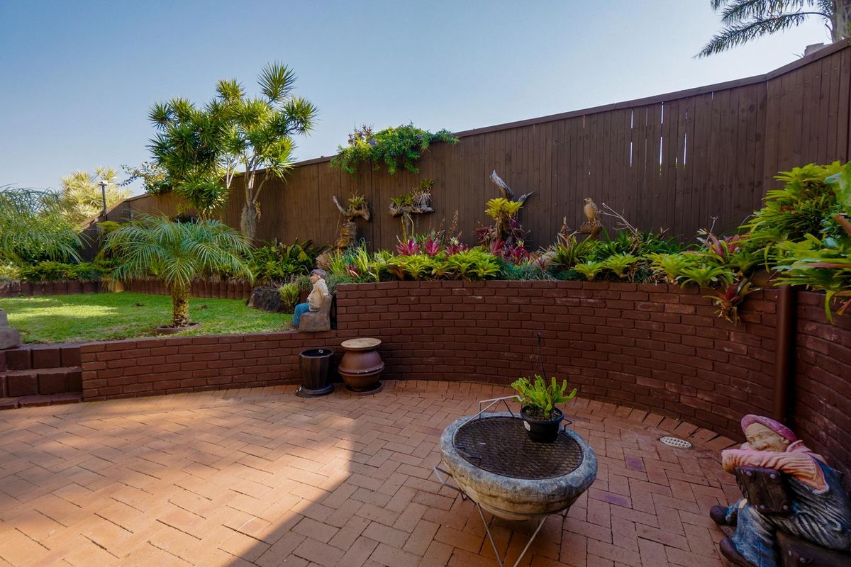 A private rear courtyard featuring brick paving, a curved brick retaining wall, and established garden beds with timber fencing.