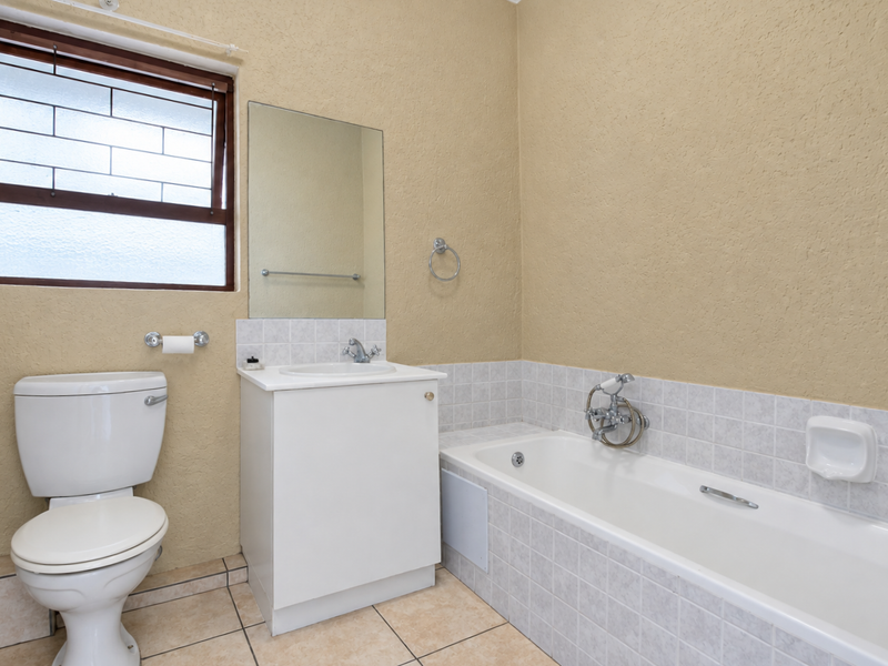 A functional bathroom featuring a white vanity, bathtub, toilet, and tiled flooring, offering a clean and neutral space ready for modernization.