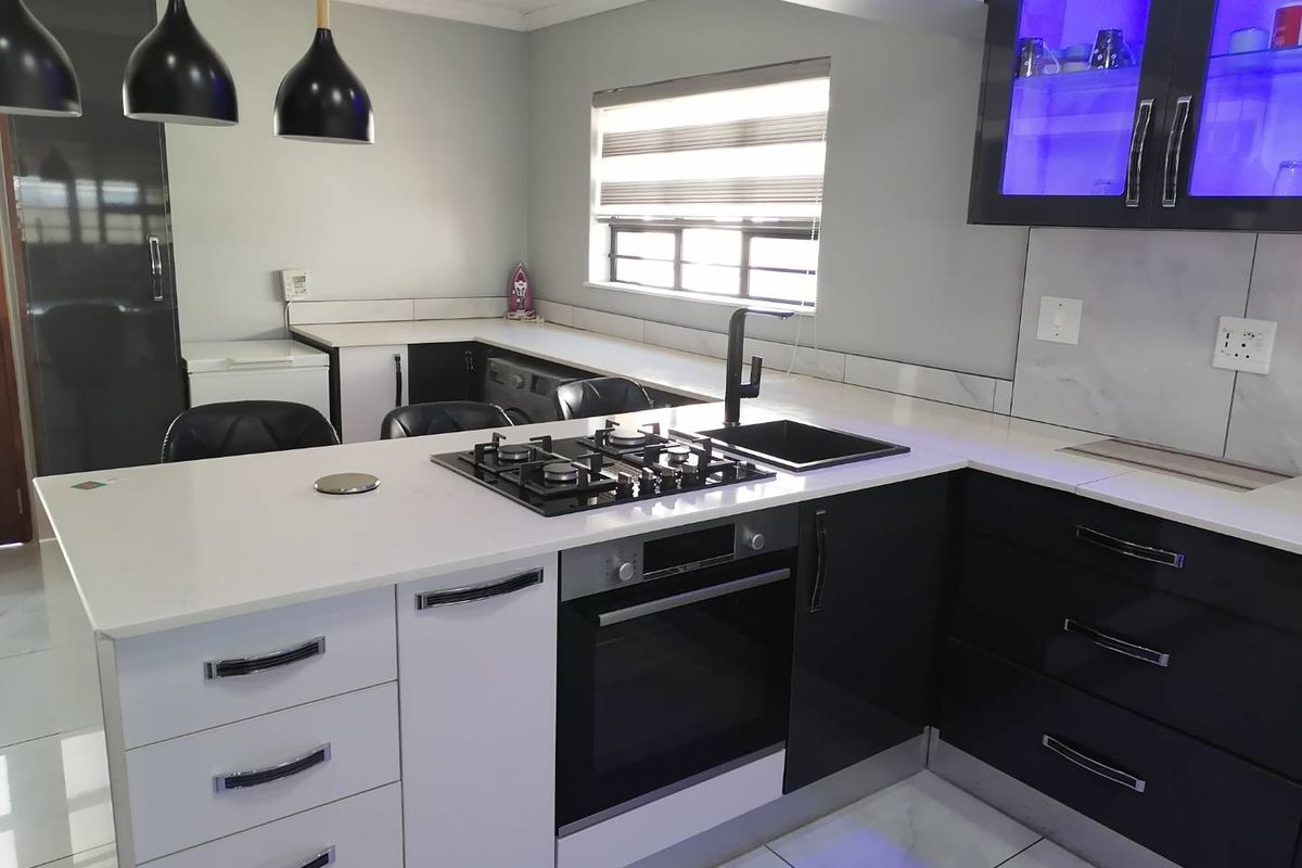Modern kitchen featuring high-gloss cabinetry, quartz countertops, a built-in oven, gas hob, and integrated lighting, offering a sleek and functional culinary space.