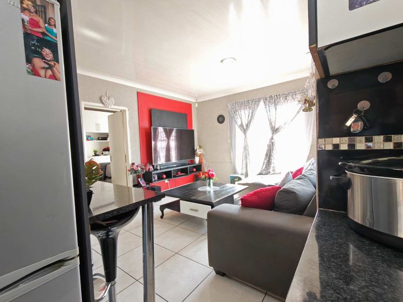 Open-plan living area featuring tiled flooring, a breakfast bar with granite countertops, and a built-in media unit, seamlessly connecting to the kitchen space.