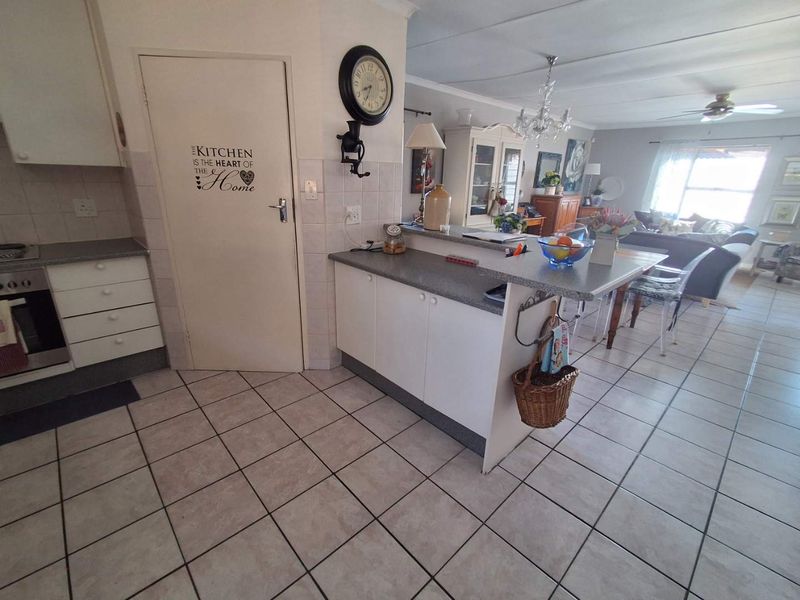 Open-plan kitchen and living area featuring tiled flooring, a breakfast counter, and built-in kitchen cabinetry with an integrated oven and hob.