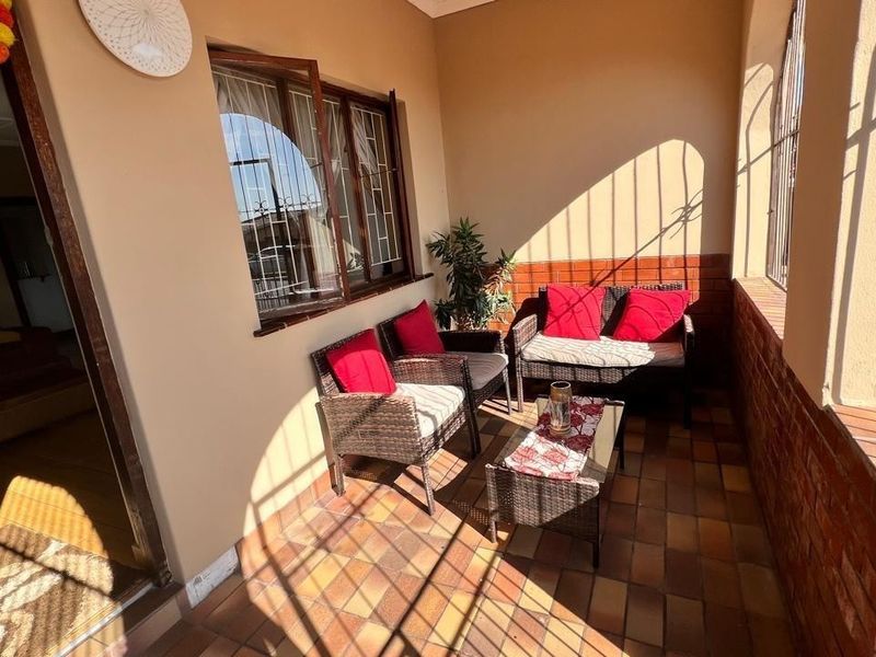 A covered patio area featuring tiled flooring, brick wall accents, and security bars on the windows, providing a functional outdoor living space.