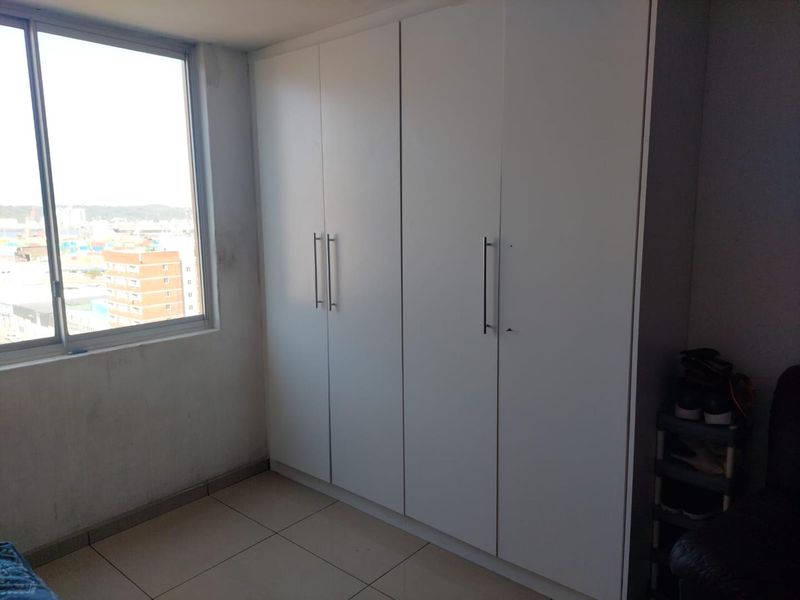 A bedroom featuring a large white built-in wardrobe, tiled flooring, and a window with an urban view.