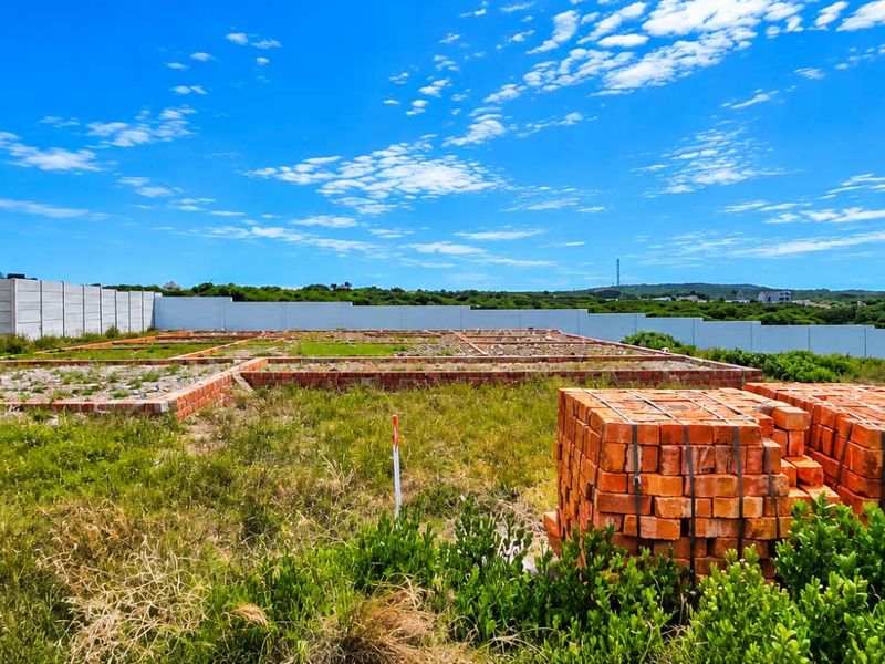 A vacant residential plot featuring a brick foundation, precast boundary walls, and adjacent building, offering a clear site for future development.