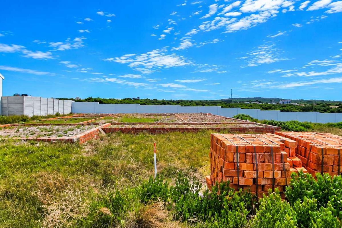 A vacant residential plot featuring a brick foundation, precast boundary walls, and adjacent building, offering a clear site for future development.