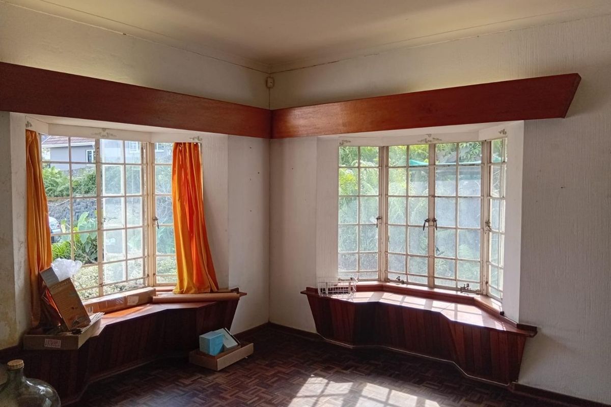 A bright, empty living room featuring classic parquet flooring, dual bay windows with timber sills, and decorative timber pelmets.