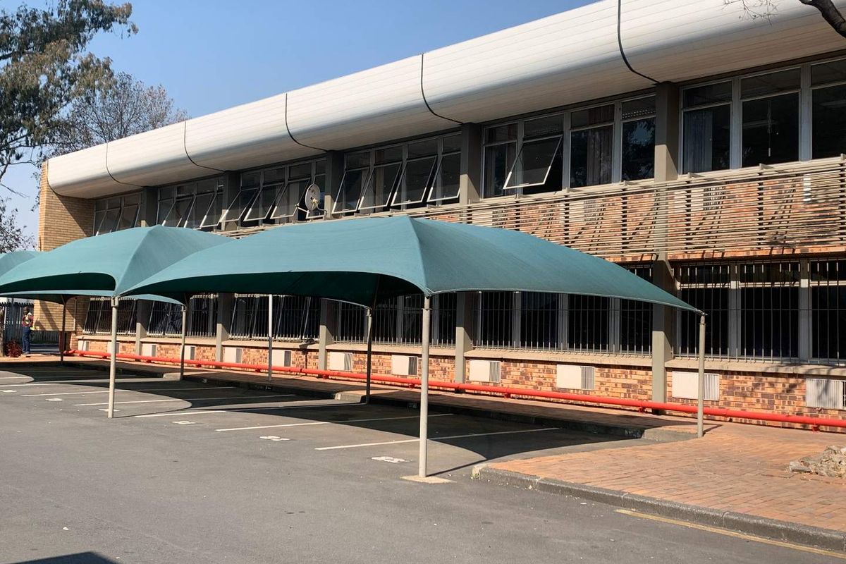 Industrial building exterior featuring brick facade, security-barred windows, and dedicated shade cloth parking bays.
