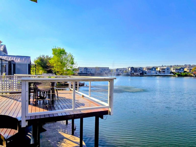 A raised timber deck patio overlooking a scenic lake, featuring a pergola and protective railing, providing an ideal outdoor entertainment space.