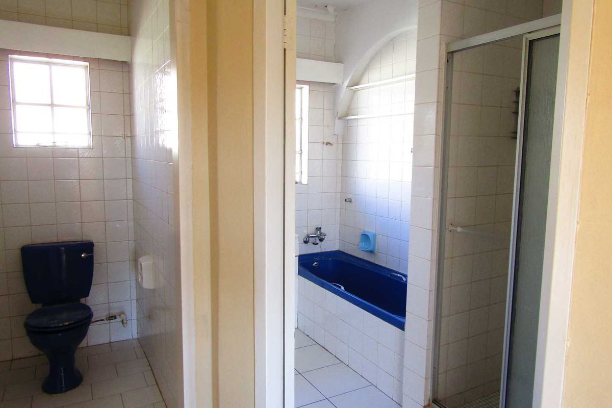 A dated bathroom featuring a blue toilet, matching blue bathtub, and a separate shower enclosure with white wall tiles.