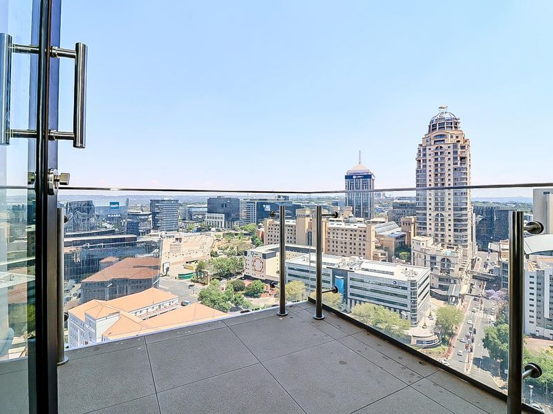 A modern balcony featuring a sleek glass balustrade with stainless steel posts, offering expansive elevated city views.