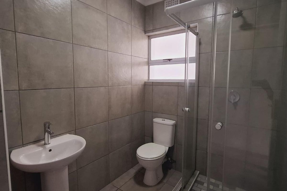A modern bathroom featuring a pedestal washbasin, a toilet, and a glass-enclosed shower with neutral floor-to-ceiling tiling.