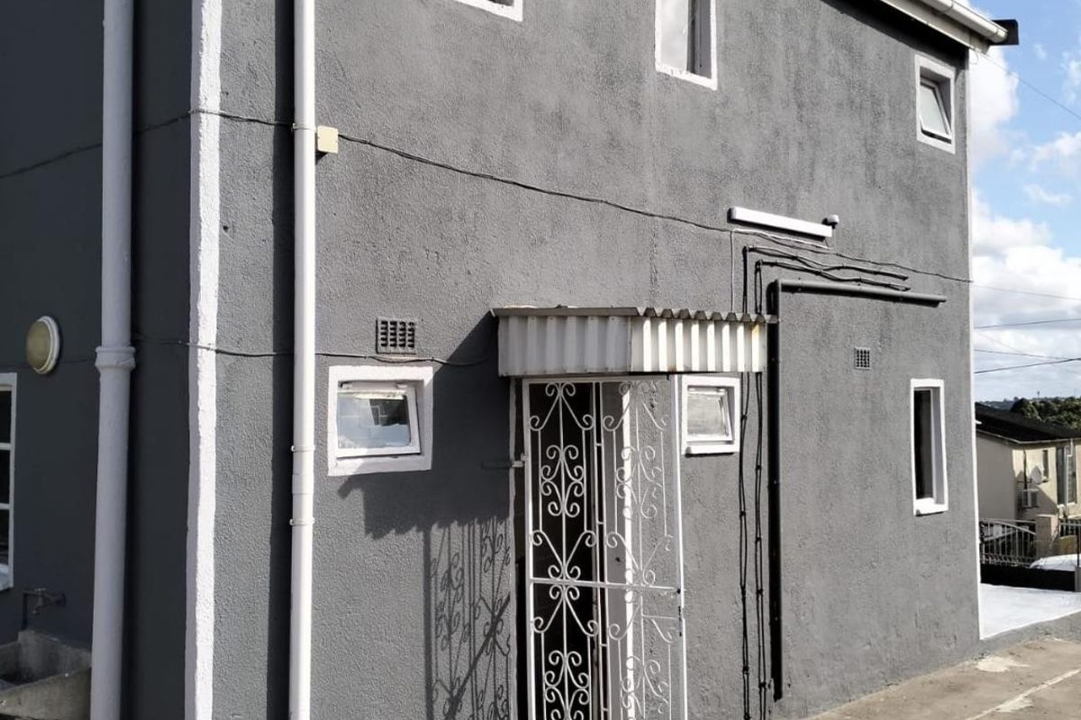 Rear exterior view of the property featuring a grey rendered facade, security gate, and a functional concrete wash basin area.