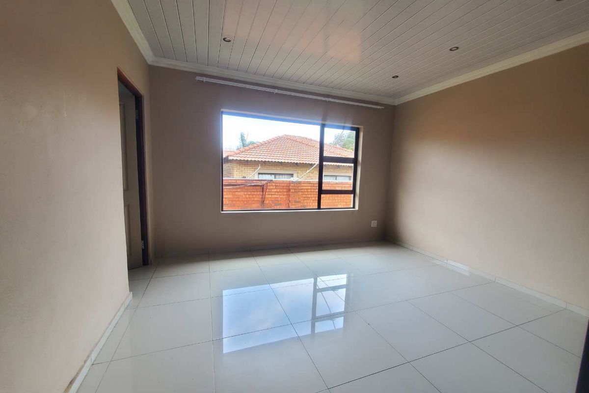 A bright, empty bedroom featuring large windows, tiled flooring, and a white tongue-and-groove ceiling.