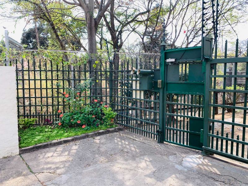 Front entrance area featuring a secure metal gate, electric fencing, and a concrete driveway with established garden border.