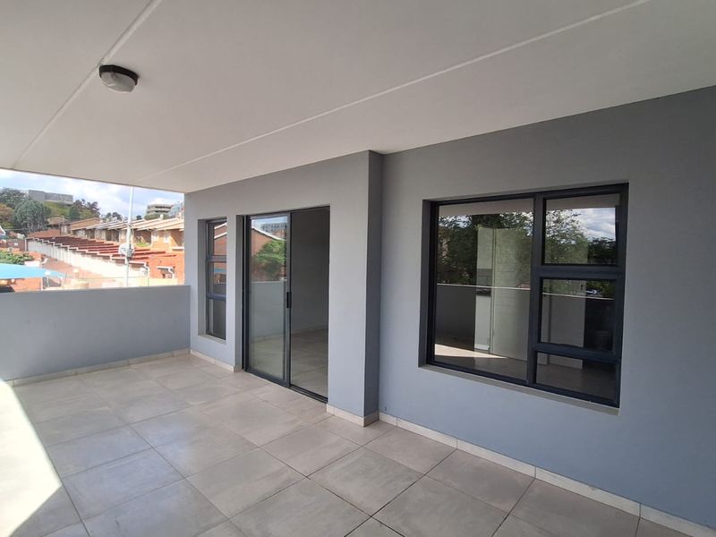 A spacious, covered balcony featuring modern grey exterior walls, large aluminium-framed windows, and neutral floor tiles, offering a clean and well-maintained outdoor living space.
