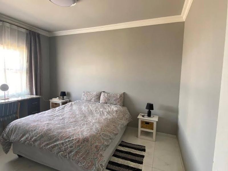 A well-lit bedroom featuring tiled flooring, crown molding, and a built-in desk area.