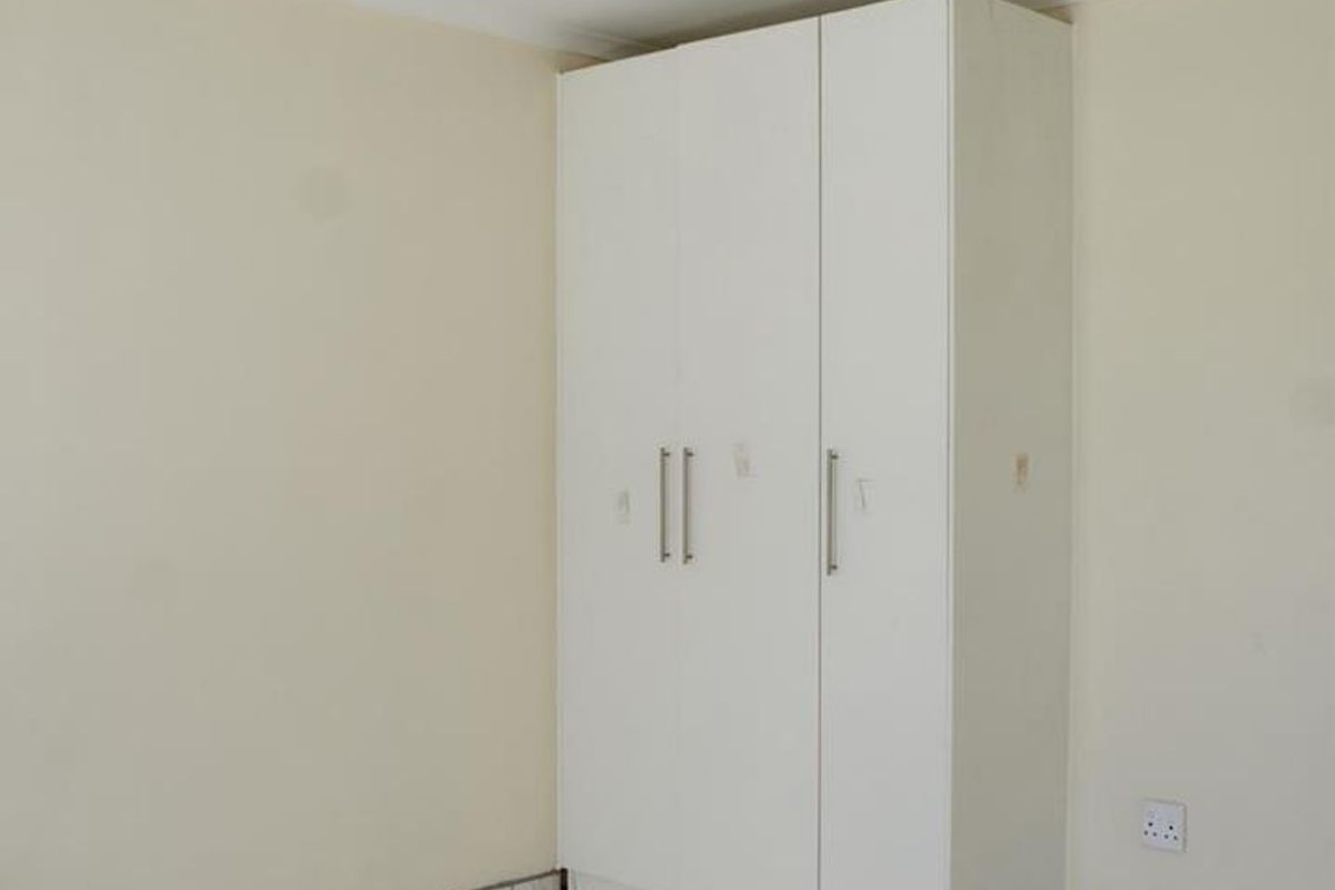 A clean, empty bedroom featuring white tiled flooring and a built-in white wardrobe.