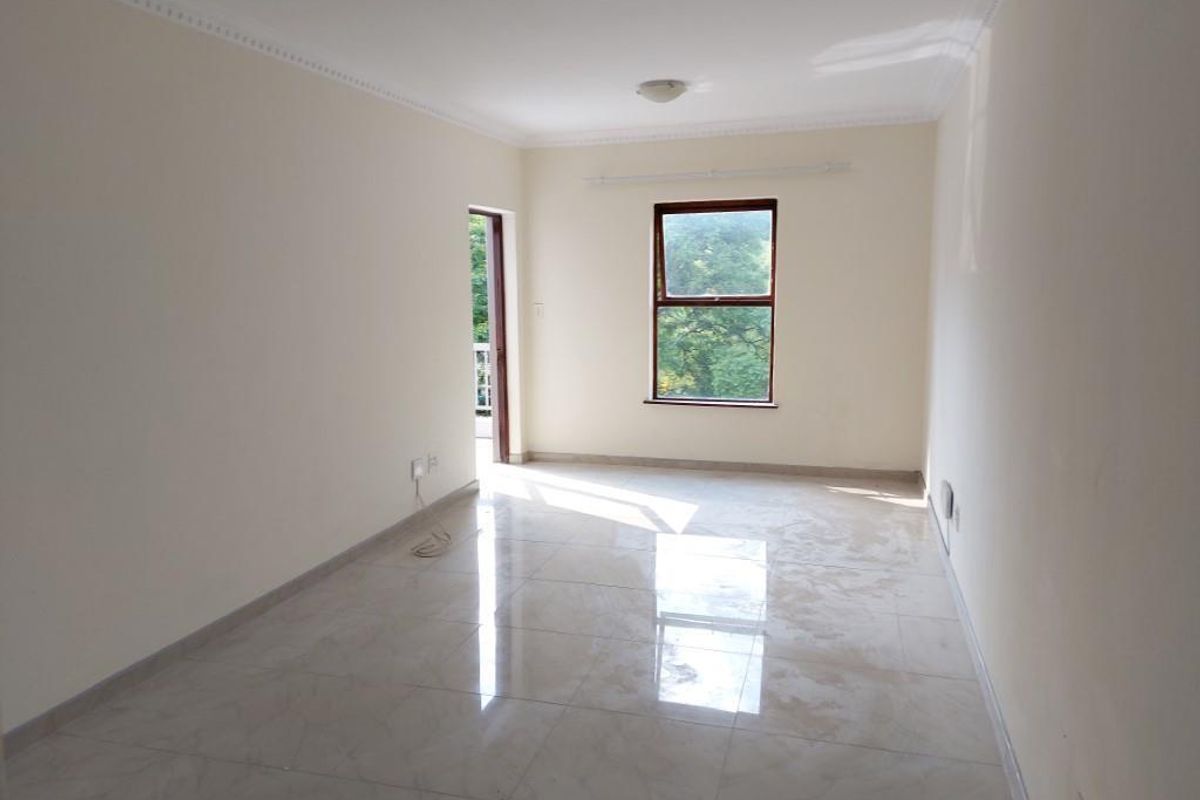 A bright, empty living room featuring polished tiled flooring, decorative cornice, and direct access to an outdoor balcony area.