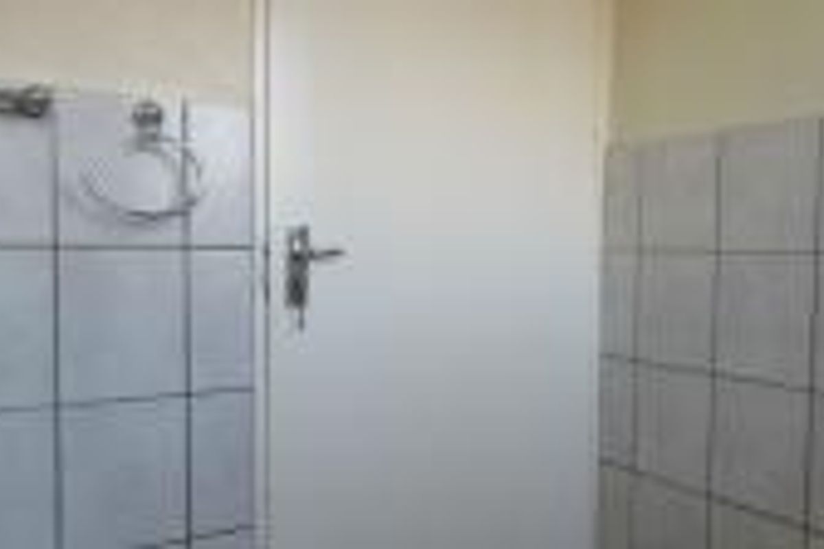 A functional bathroom space featuring tiled walls, a towel ring, and a towel rail, currently in need of cosmetic updates.